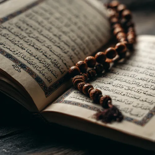 نمای نزدیک از صفحه قرآن با تزیینات سنتی و تسبیح چوبی قرارگرفته روی خطوط آیات.